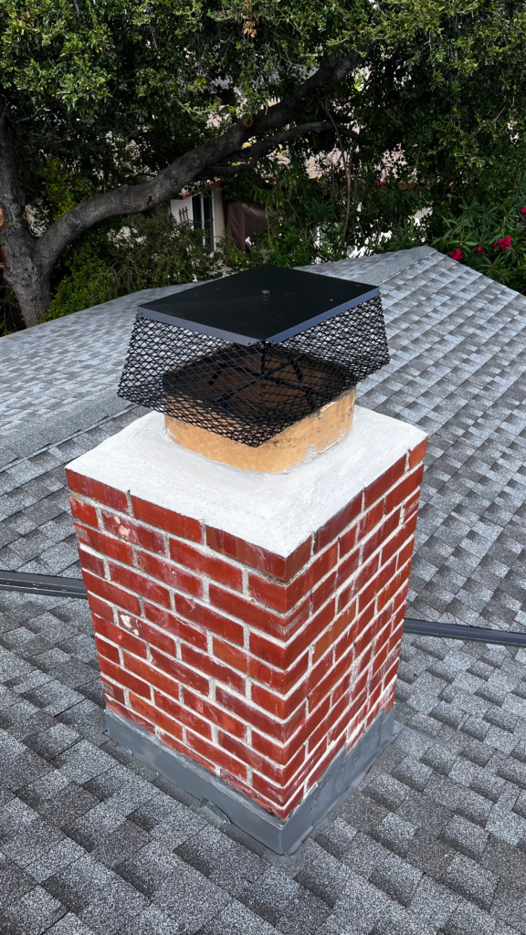 Red brick chimney with black chimney cap installed on residential roof in Fremont CA